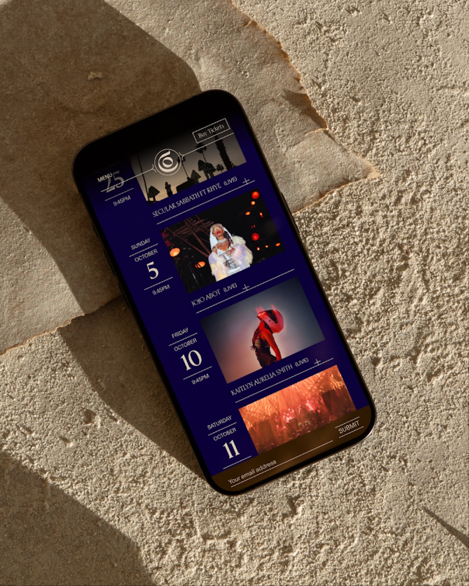 Mobile phone display shows event schedule with performers on dark blue background with soft lighting and natural stone surface.
