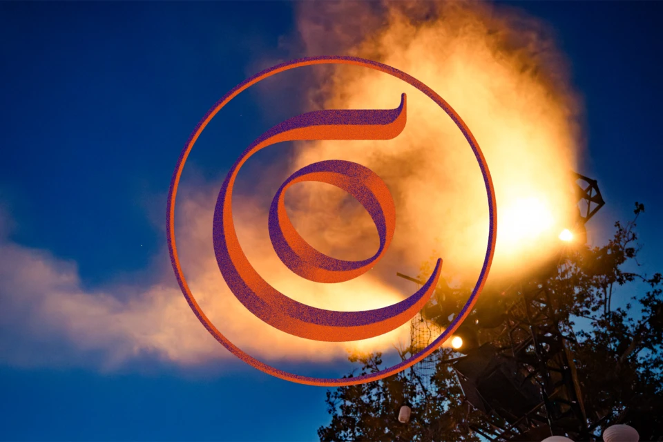 Abstract orange and purple logo against a night sky with bright stage lights and clouds, creating a dynamic visual.