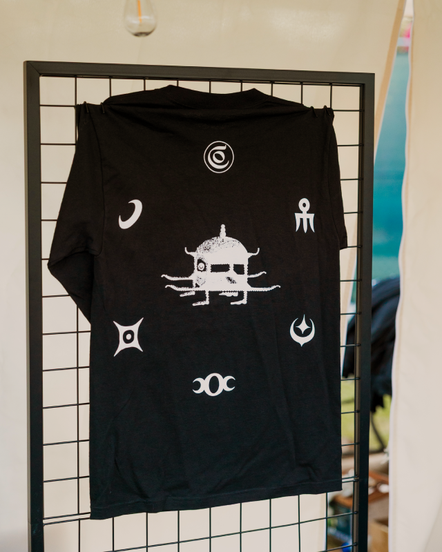 Black long-sleeved shirt displayed on a wire rack, featuring white graphic designs including an abstract figure and various symbols.
