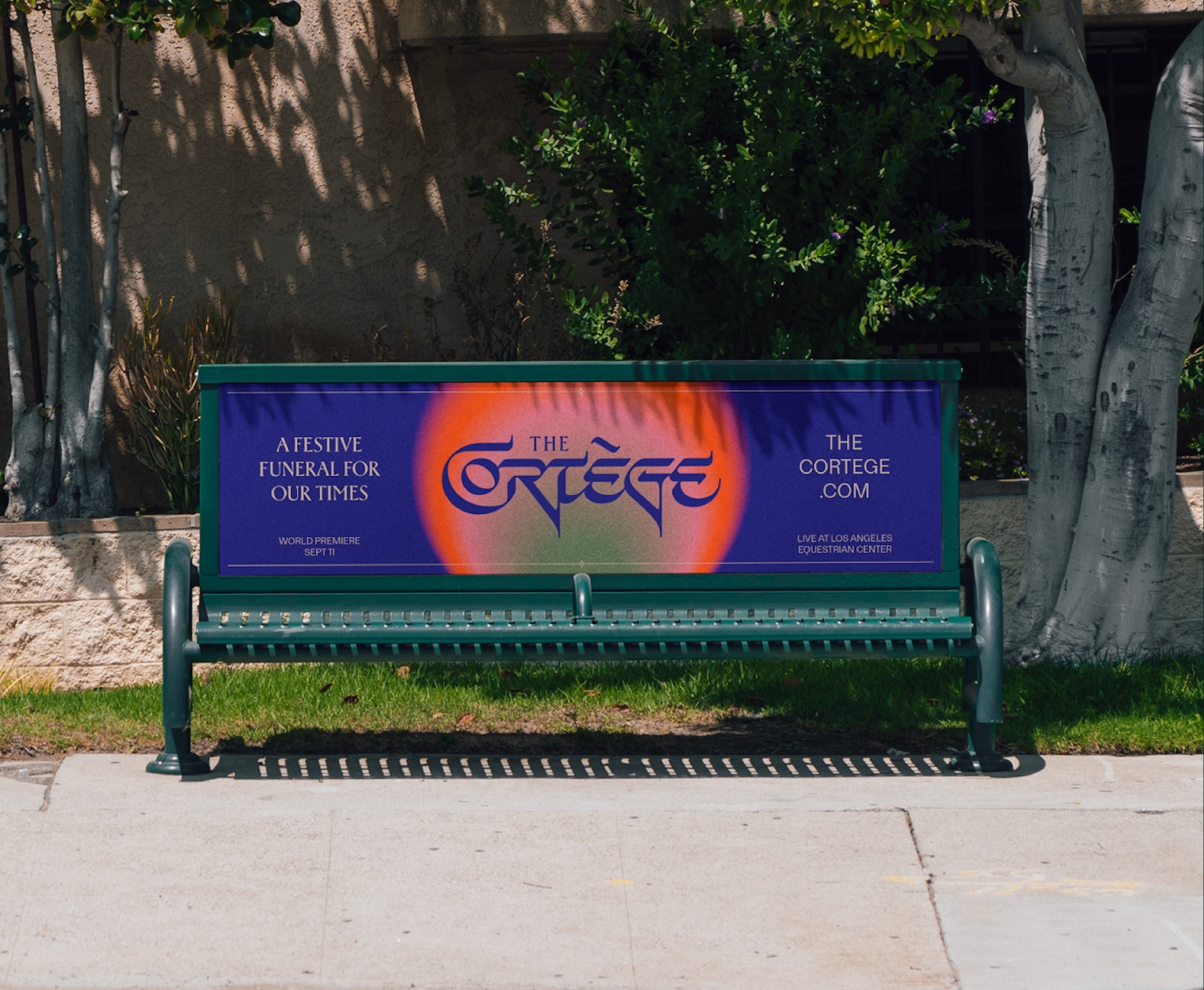 Outdoor shot of a green metal bench with a blue advertisement featuring a stylized orange graphic and white text.