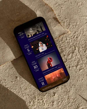 Smartphone displaying a dark UI event schedule resting on a textured natural stone surface