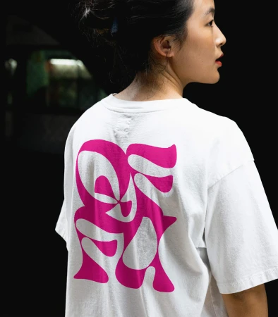 Woman in white t-shirt with abstract pink design stands against dark background. Focus on t-shirt graphic.