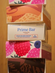 A vertically stacked tower of five colorful product packaging boxes with illustrated fruit and abstract designs against a plain wood background.