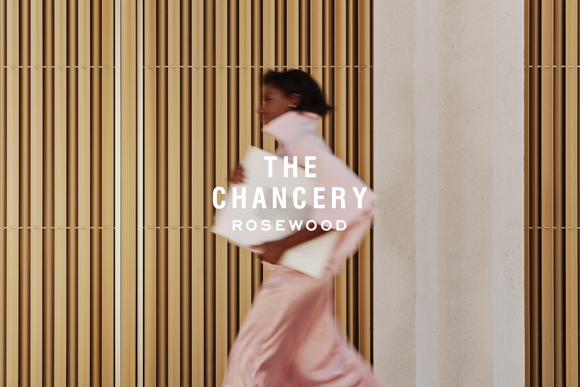 Motion blurred woman walking past ribbed wooden wall carrying white panels for Rosewood brand identity project