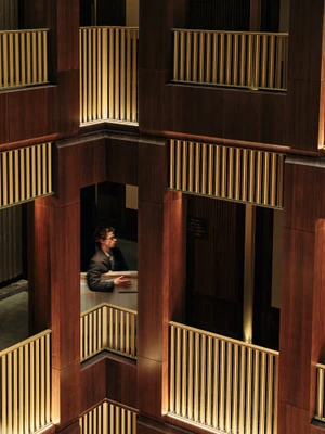 Man standing on a multi-level hotel balcony with dark wood paneling and gold-toned railings