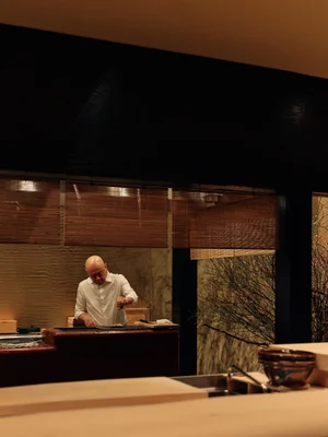 Chef in white shirt working in a dimly lit restaurant kitchen with wooden blinds