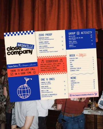Menu board for Nashville's Close Company featuring cocktail and beer listings, held in front of patrons in a dimly lit setting.
