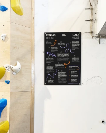 Indoor climbing gym rules posted on a sign. The sign has the rules written in both English and Portuguese, using arrows and lines to guide the eye.