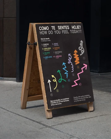 Sidewalk sign with motivational message in Portuguese and English, featuring colorful arrow illustrations representing various emotional states.