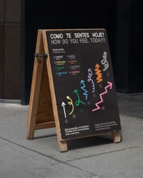 A-frame wooden sandwich board sign on a concrete pavement featuring a black chalkboard display with colorful arrows and text.