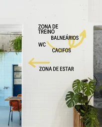 White tiled wall with black directional typography and yellow arrows pointing toward different facility zones