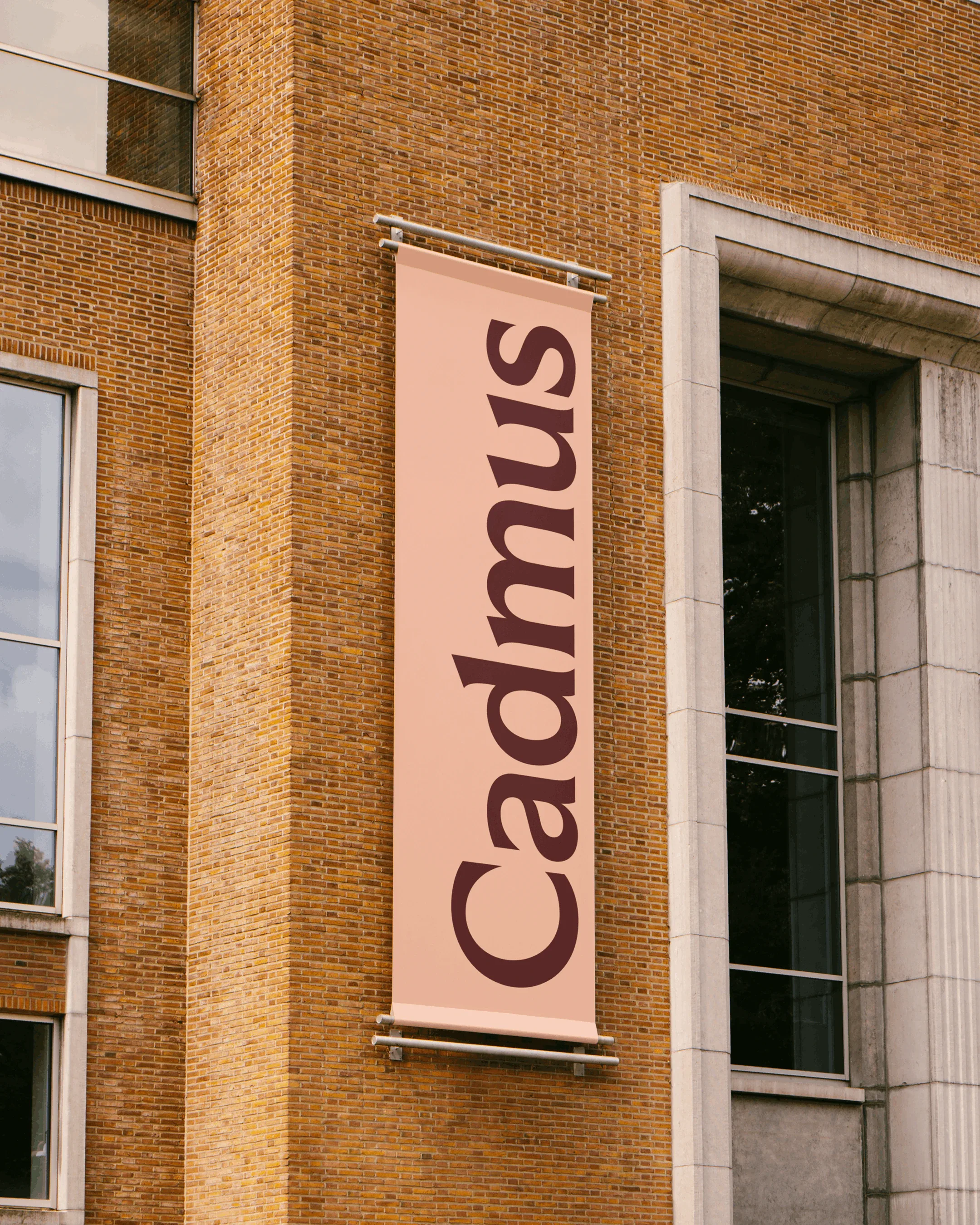 Architectural shot of a tall brick building featuring a vertically-oriented banner with the text 'Cadmus' on its side.