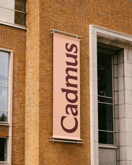 Architectural shot of a tall brick building featuring a vertically-oriented banner with the text 'Cadmus' on its side.
