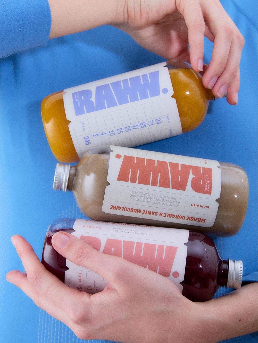 Three bottles of juice by RAW are held by a person in a studio setting, showcasing a trio of vibrant, refreshing, and healthy drinks.