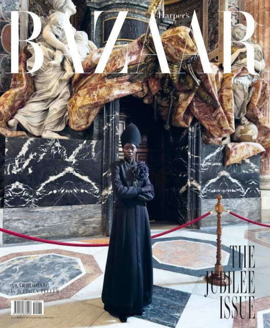 Model wearing a long black coat and matching headdress standing before classical marble architecture for Harpers Bazaar Italia.