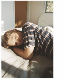 Model lying on a bed wearing a striped short-sleeve top in a domestic bedroom setting by Madewell.