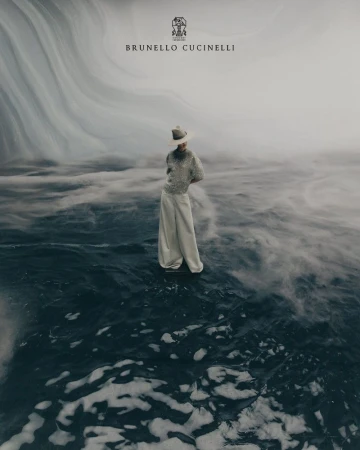 A woman stands in wide-leg pants and a shimmering top against an abstract water backdrop, logo of Brunello Cucinelli is on top.