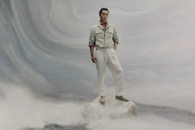 Full-length portrait of a male model posing on a rock formation against a swirling abstract marbled background for Brunello Cucinelli.
