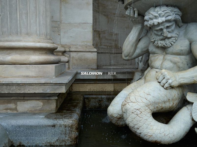 Architectural sculpture of a merman seated alongside a column with water flowing, captured in neutral tones, and classical style.