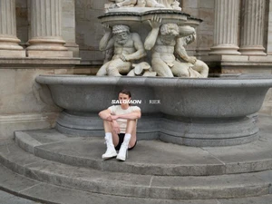 Man seated on stone steps in front of a classical stone fountain for the RIER x SALOMON campaign.