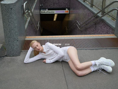 Model lying on concrete ground near subway station stairs wearing white long-sleeve top and sneakers