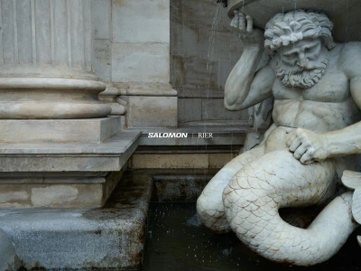 Close-up of a carved marble fountain sculpture featuring a bearded male figure beside classical architectural columns.