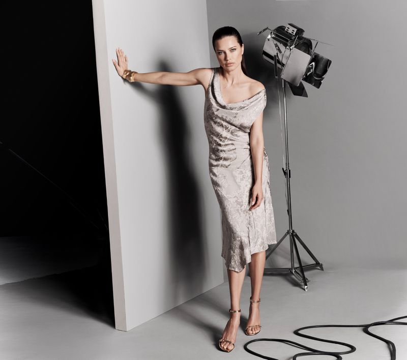 Woman in a draped silver dress posing in a photo studio with a large studio light and grey background.