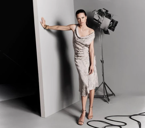 Woman in a draped silver dress posing in a photo studio with a large studio light and grey background.