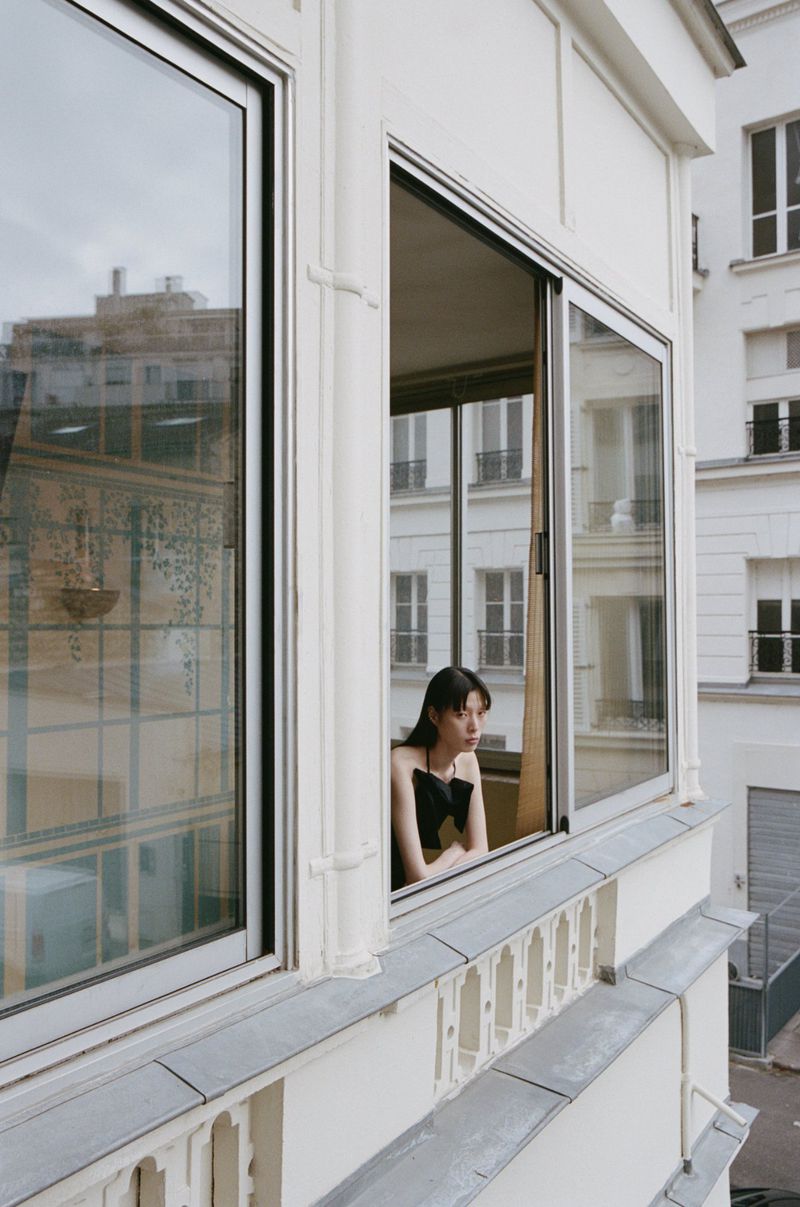 Woman leaning on an open window frame of a white building exterior