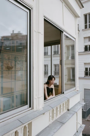 Woman leaning on an open window frame of a white building exterior