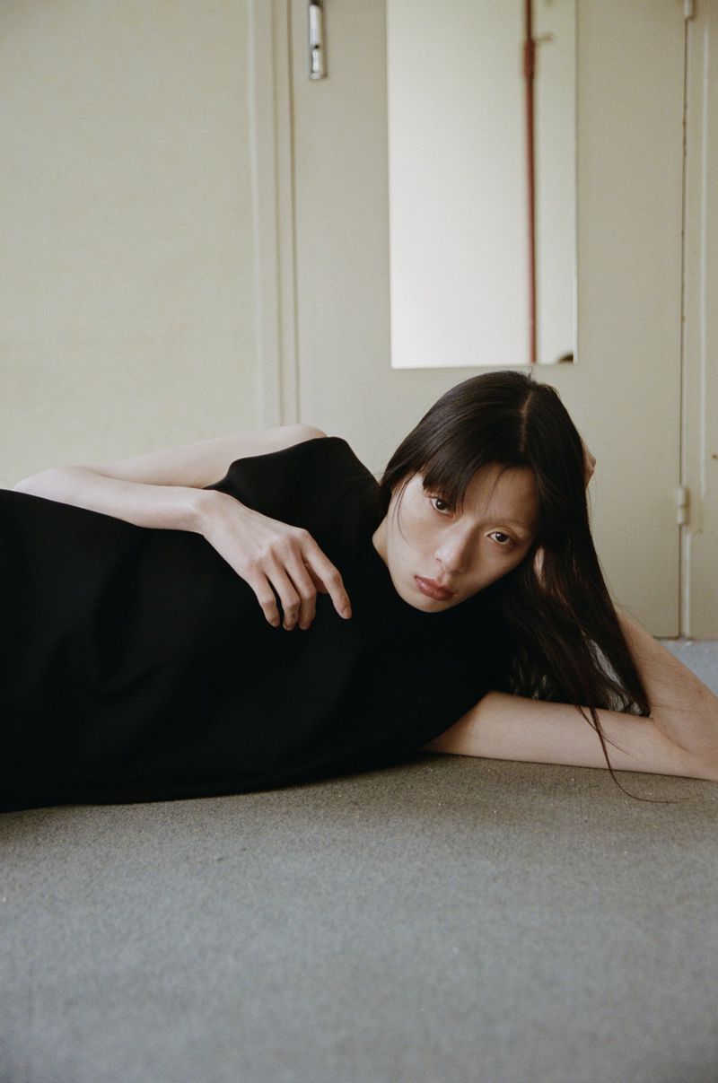 Model in black sleeveless top lying on a carpeted floor in an indoor hallway setting
