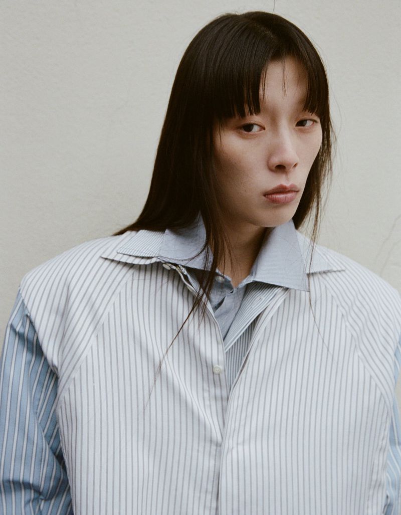 Headshot of a young Asian woman with long dark hair wearing a blue button-down shirt and pinstripe vest looking directly at the camera.