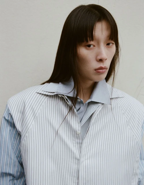 Headshot of a young Asian woman with long dark hair wearing a blue button-down shirt and pinstripe vest looking directly at the camera.
