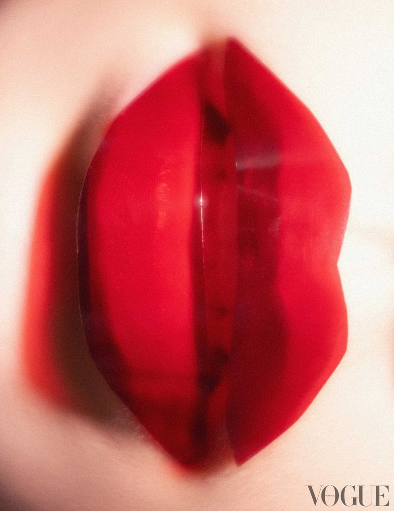 Close-up of luscious, glossy red lips with soft skin, captured in a vibrant, high-fashion beauty shot with 'Vogue' logo at the bottom.
