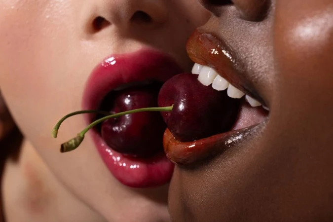 Close-up of two models holding fresh cherries between their glossy lips for Vogue Portugal