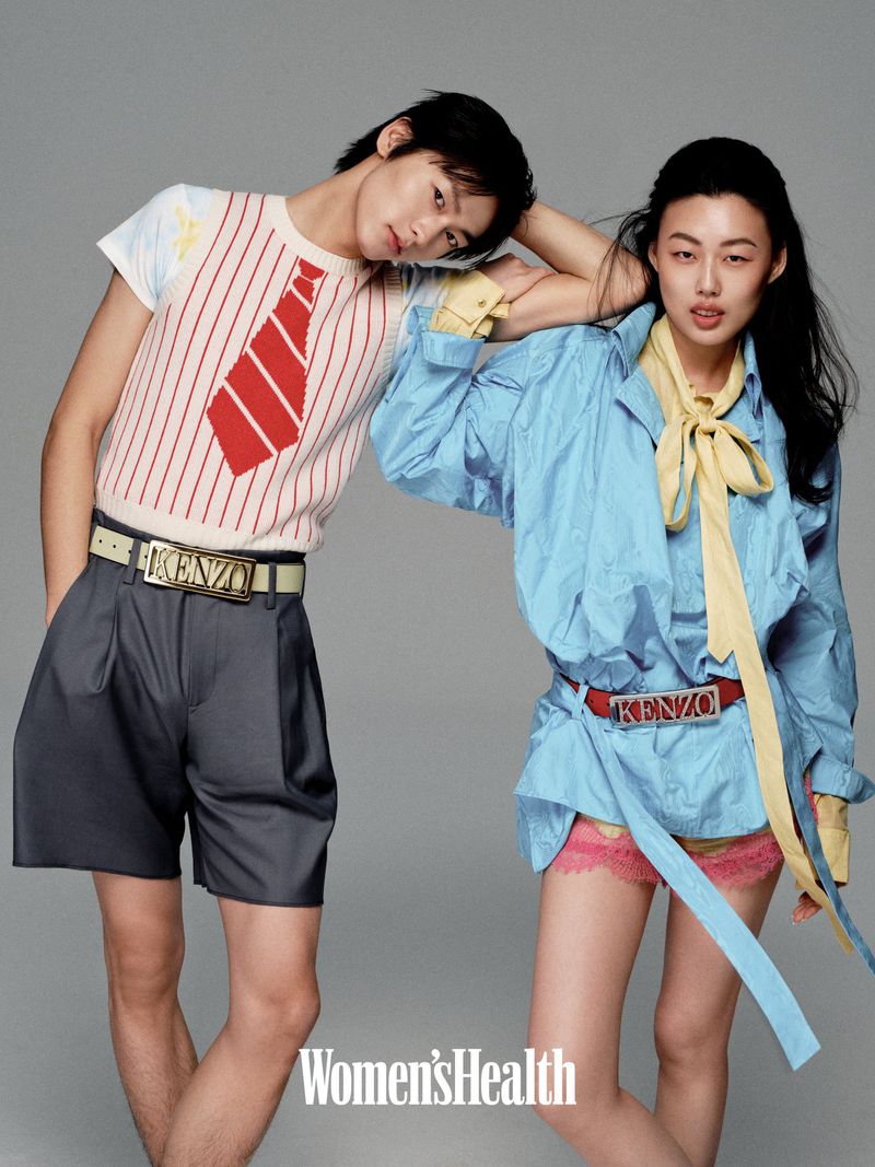 Two Asian fashion models strike a pose in a studio, the man wearing a white shirt with red tie, the woman a blue top and matching belt.