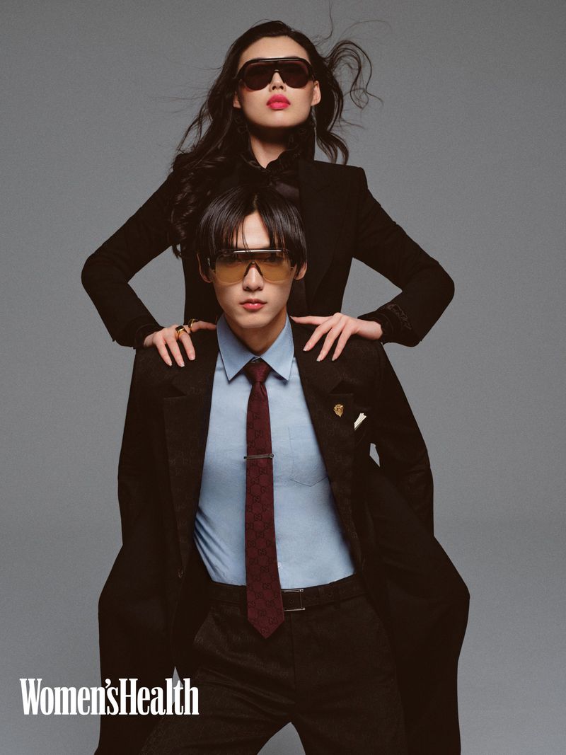 Two Asian models in retro sunglasses posing in a studio setting. One model is wearing a black coat while the other is wearing a suit.
