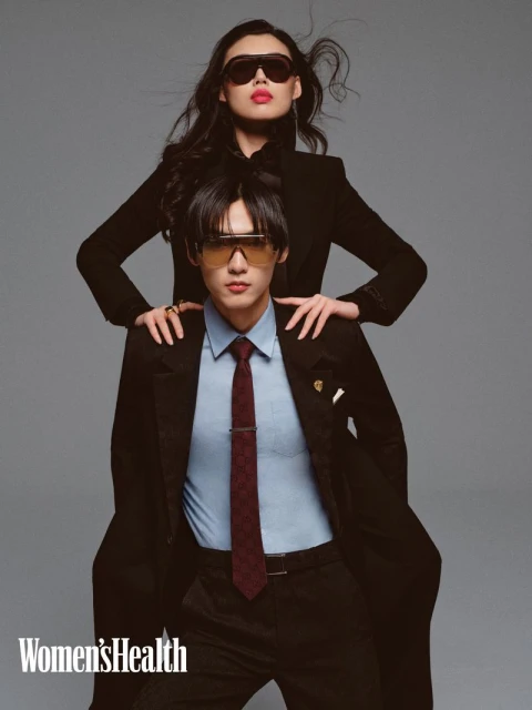 Two Asian models in retro sunglasses posing in a studio setting. One model is wearing a black coat while the other is wearing a suit.