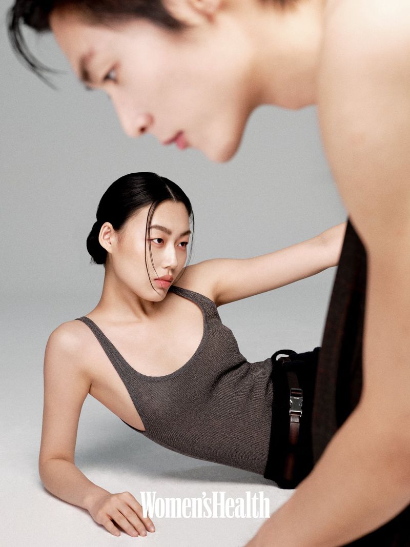 Attractive diverse couple poses intimately together in a studio, the woman in a fitted bodysuit with the man partially in the shot.