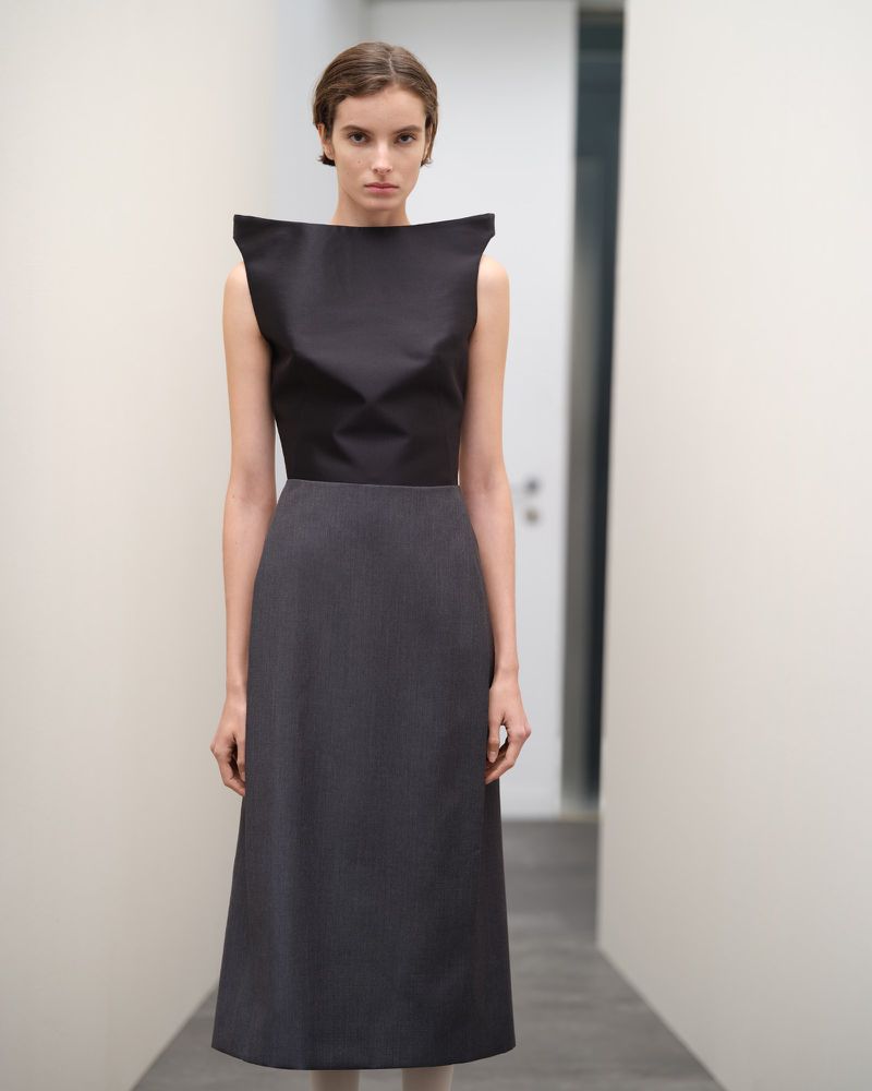 Elegant woman in a black and grey dress stands in a bright, minimalist hallway, showcasing modern fashion with clean lines and neutral tones.