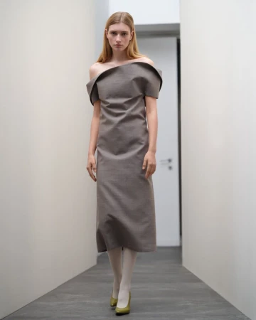 Model wearing an off-the-shoulder grey midi dress walking down a hallway for Jil Sander