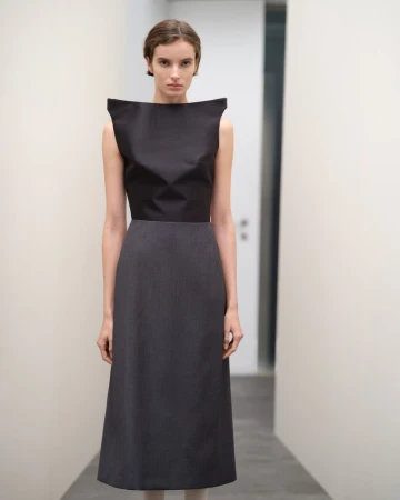 Model wearing a structured black boatneck top and grey midi skirt in a minimal hallway