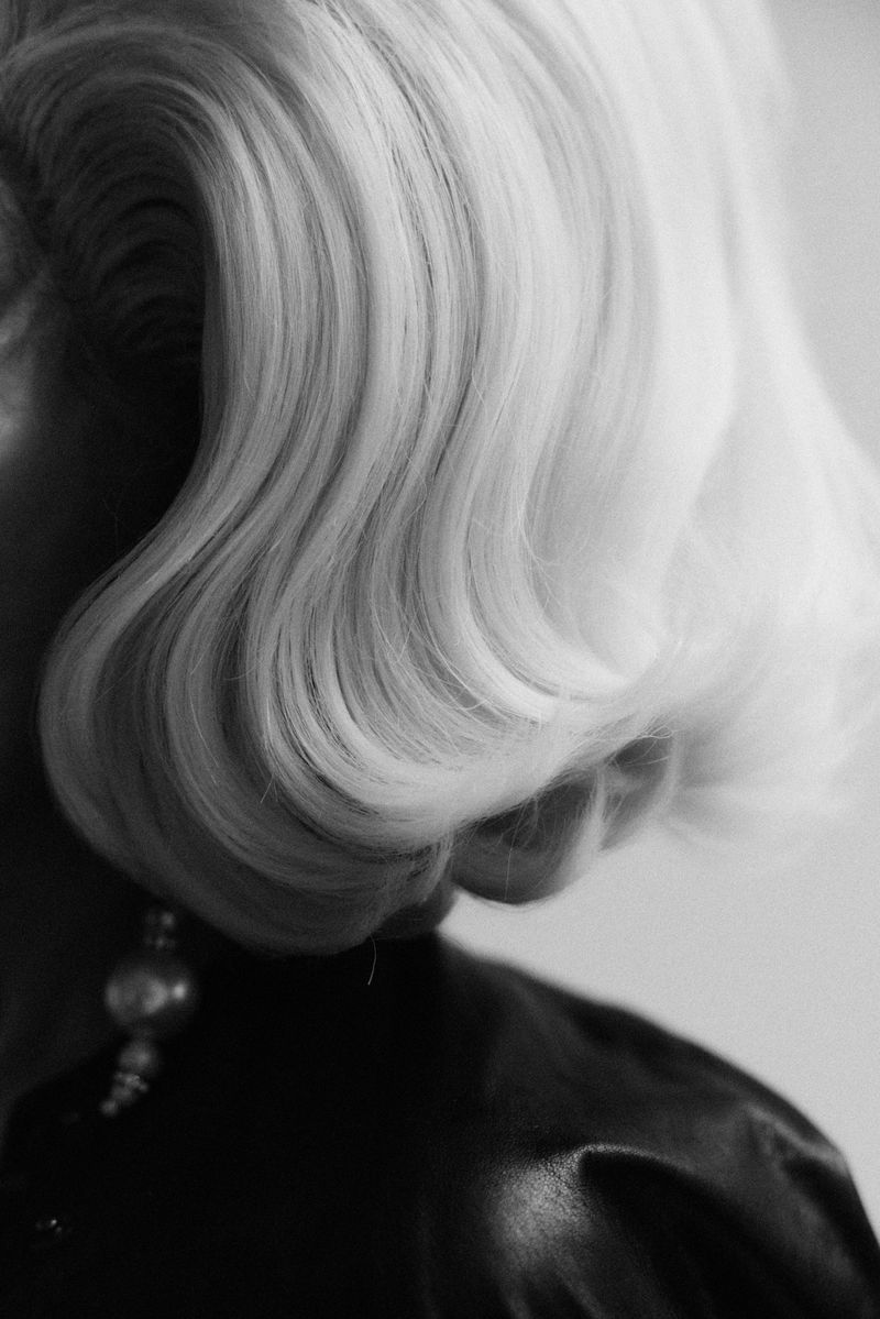 Black and white close-up of an adult female with blonde wavy hair wearing a dark top and an earring. Soft light.