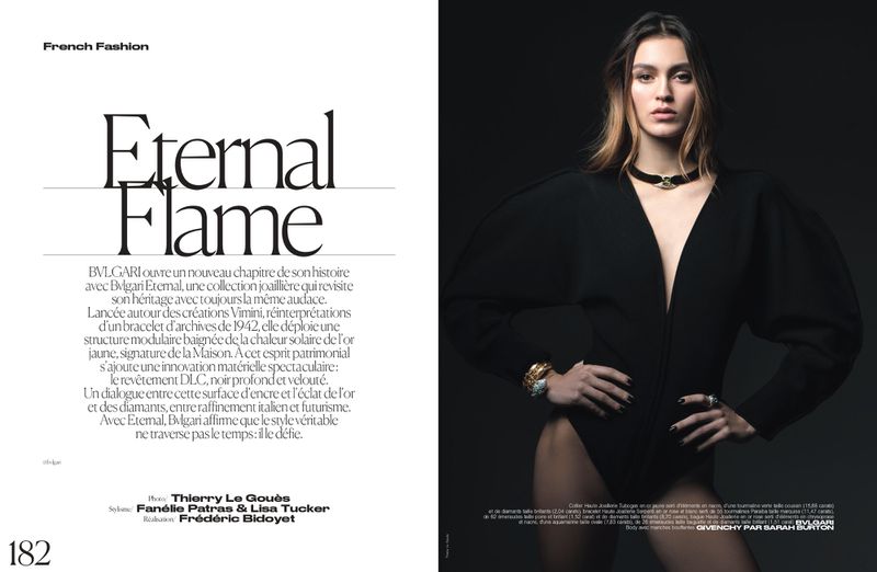 Fashion shot of a woman wearing a black bodysuit and jewelry, posing against a dark background in a studio setting. Editorial fashion photography.