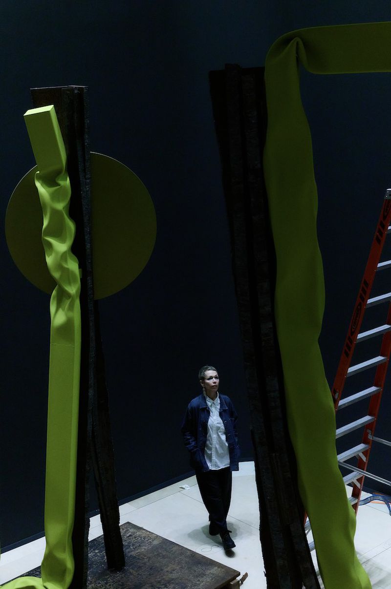 Woman in gallery looking at abstract sculpture with lime-green fabric wrapped around dark posts with a lime-green circle element.