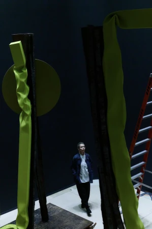 Woman in gallery looking at abstract sculpture with lime-green fabric wrapped around dark posts with a lime-green circle element.
