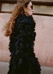 Woman in textured black coat wearing sunglasses and gold earrings outdoors for Elle Canada