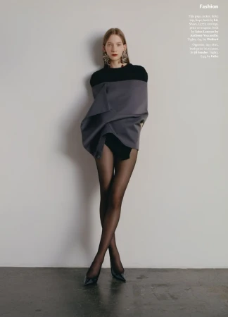 Fashion editorial shot of a young adult female fashion model wearing a black bodysuit, gray sweater, black tights, and black high heels.