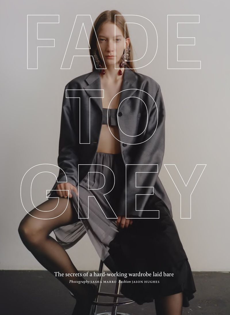 Fashion editorial image features a seated woman wearing a grey blazer, matching crop top, and pants with long dark hosiery and statement earrings.