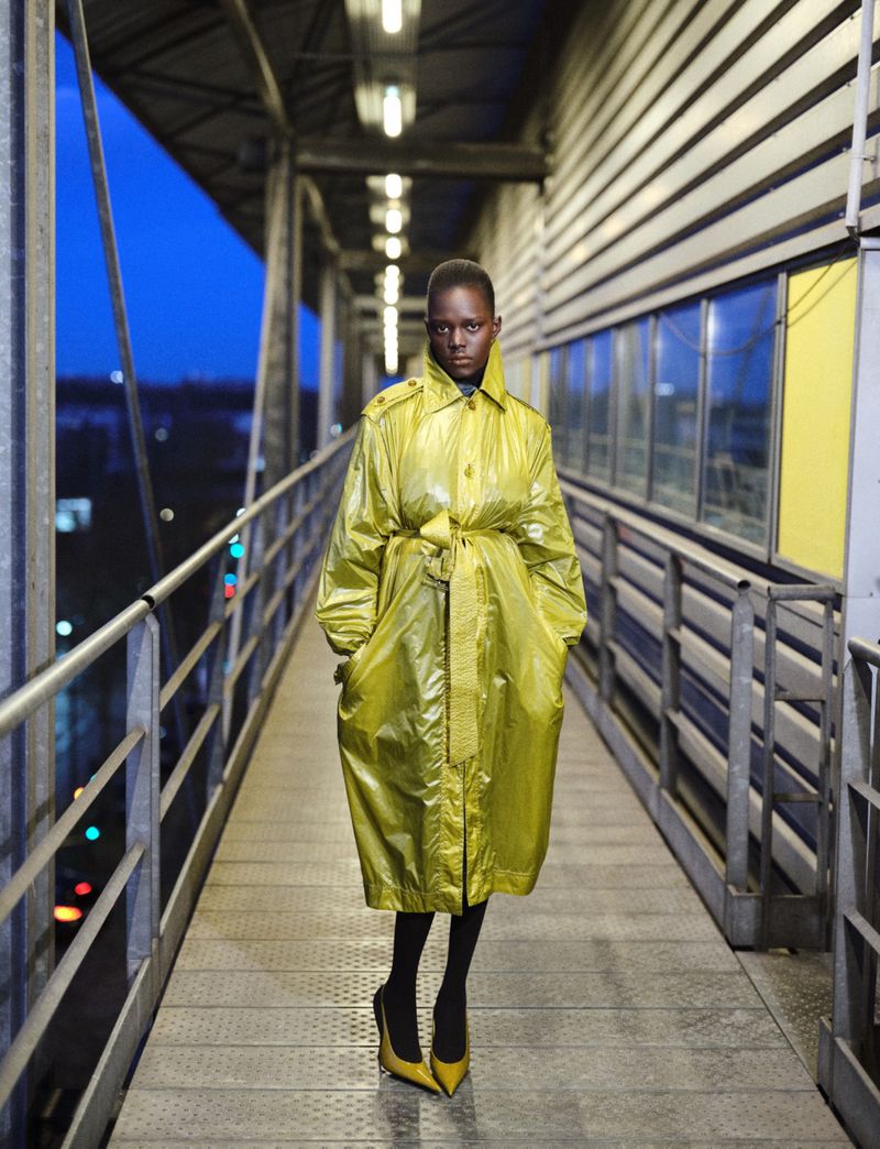 Fashion shot: Woman in a yellow trench coat and matching heels on a pedestrian bridge at dusk, creating a striking and modern image.